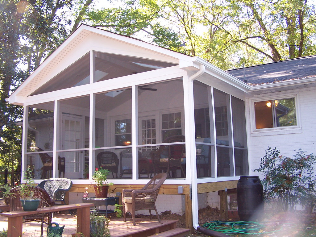 A white-framed screened porch on the back of a house, with patio furniture visible through the mesh